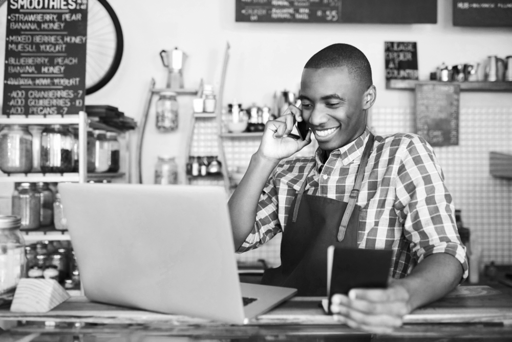 Young business man in a stripey shirt looking at his laptop smiling in a cafe environment